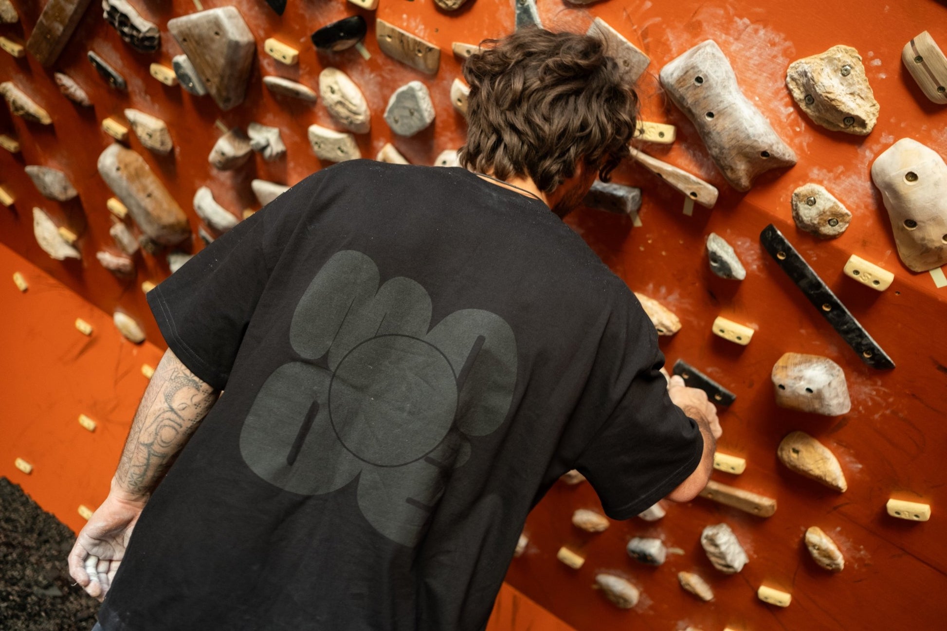 Person climbing on a rock wall with a black t-shirt featuring a logo.